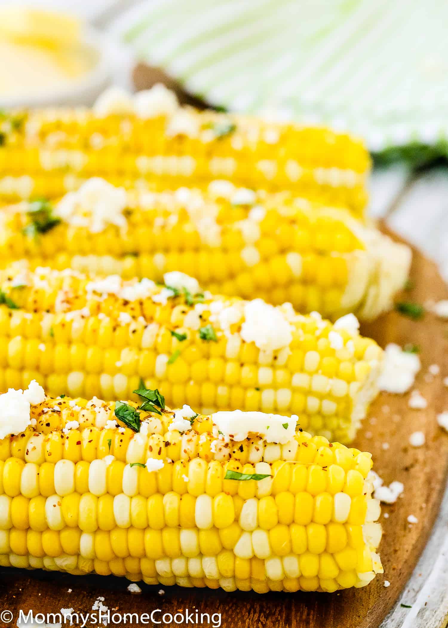 close up view of fresh corns on the cob over a wooden tray with crumbled queso fresco, butter and tanjin. 