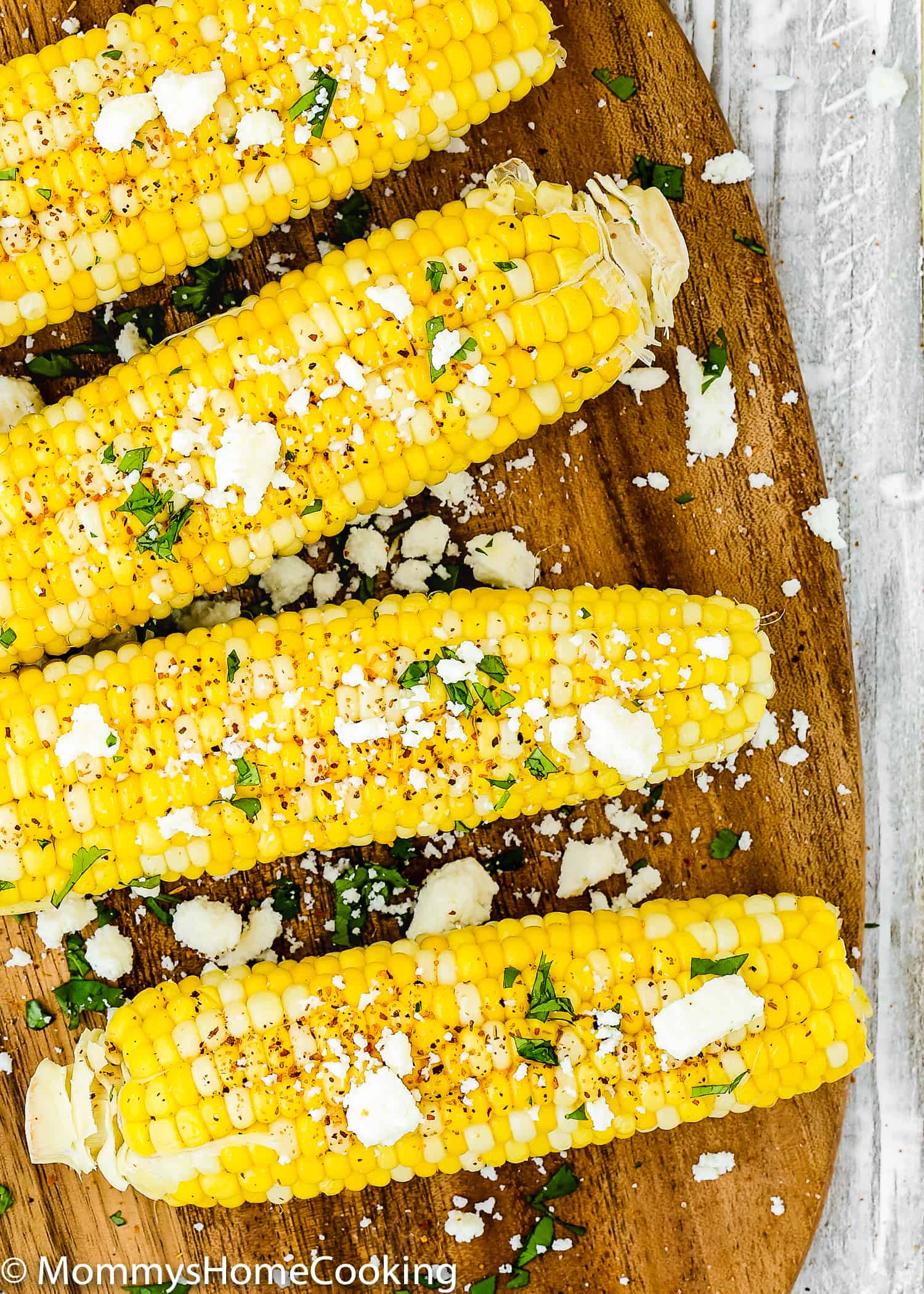 fresh corns on the cob over a wooden tray with toppings. 
