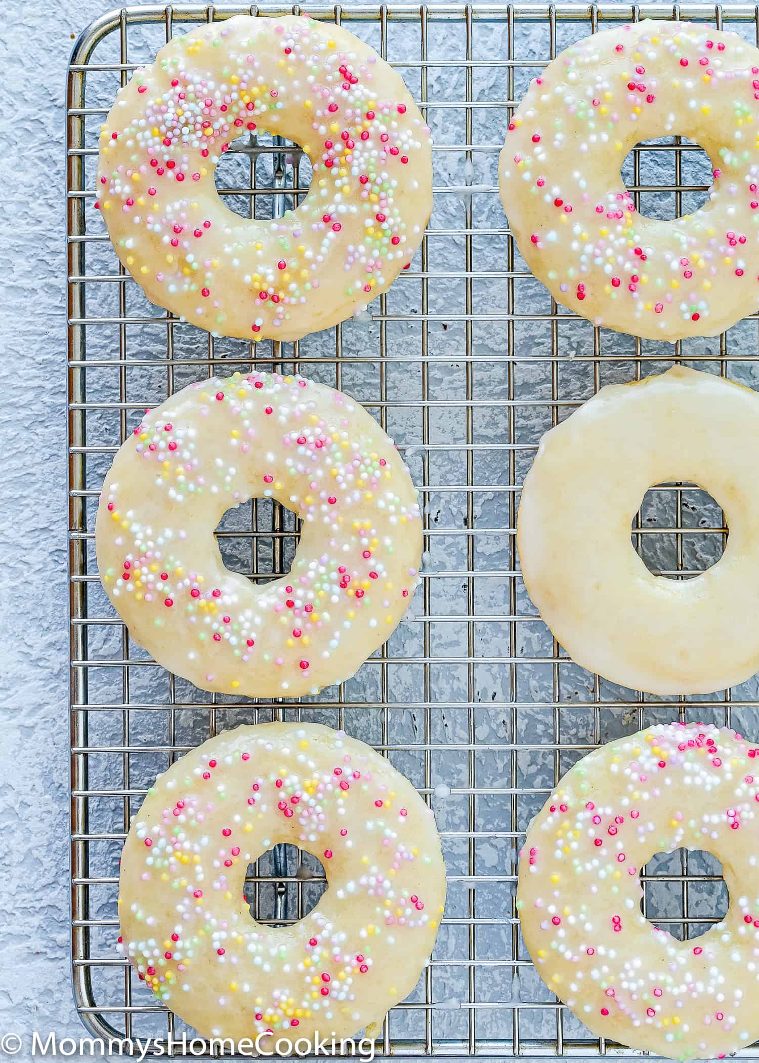 Overhead view of six glazed baked egg-free donuts with five with sprinkles on top.
