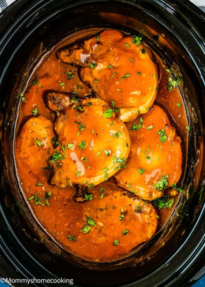 Slow Cooker Beer Pork Chops with chopped parsley in a slow cooker.