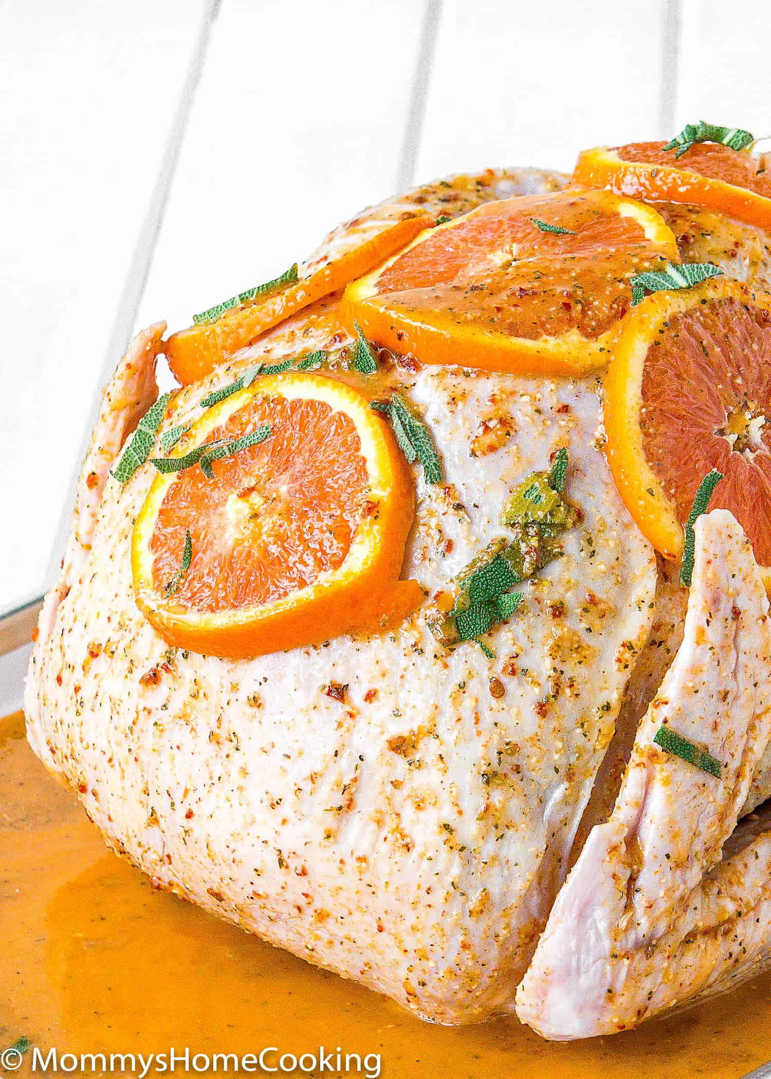 close up view of a raw turkey with citrus chipotle marinade with orange slices and herbs on top