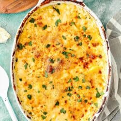 Cheesy Potatoes and Cod Casserole over a blue surface with a serving spoon on the side.