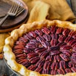 egg-free pecan pie in a pie dish on a wooden surface with plates, forks and napkin on the background