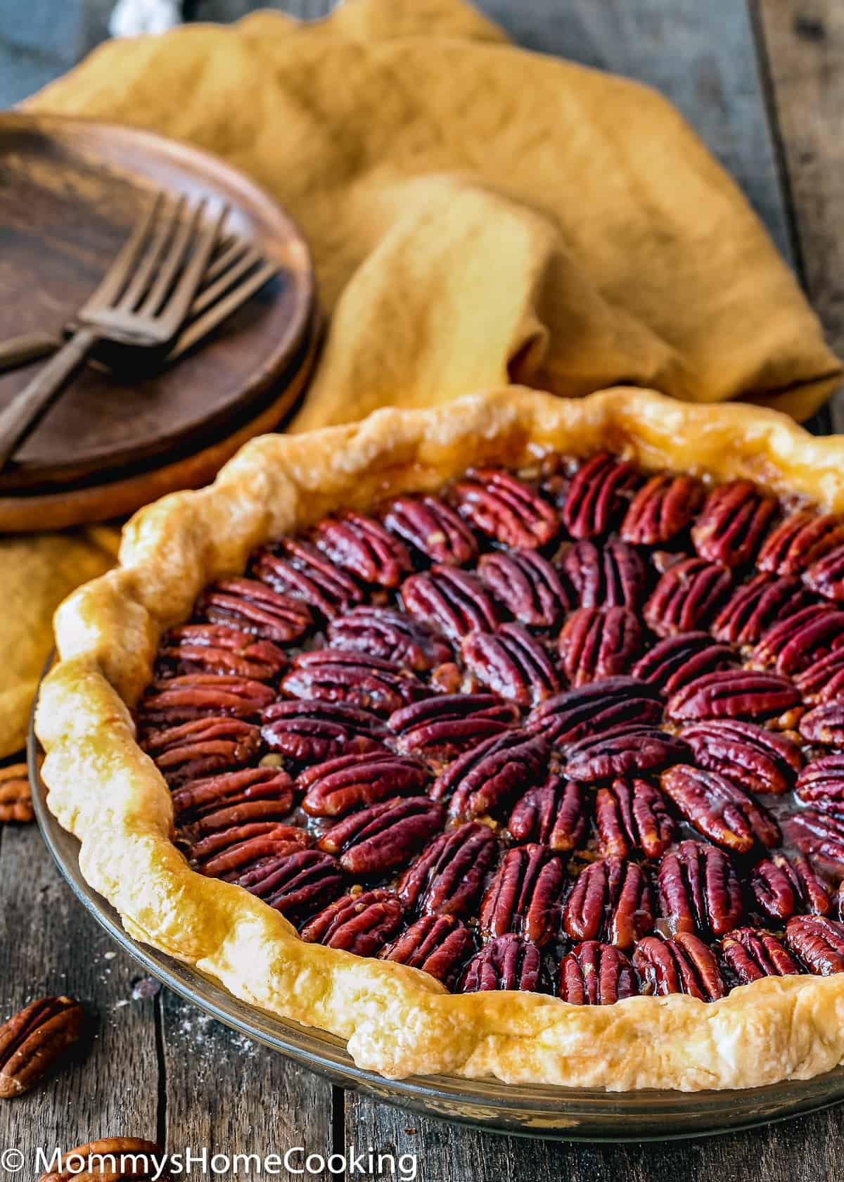 egg-free pecan pie in a pie dish on a wooden surface with plates, forks and napkin on the background 