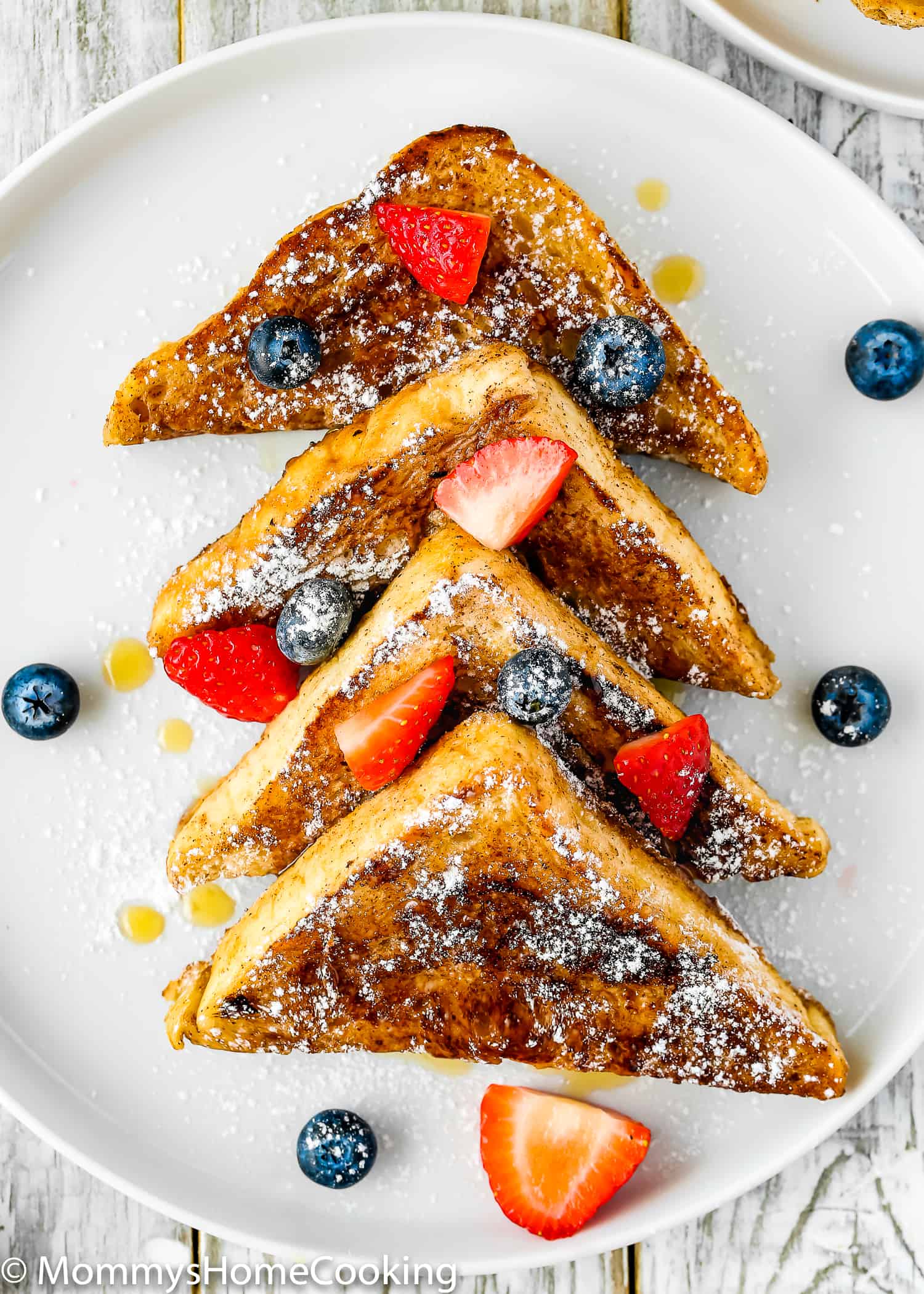 A platter of French toast cut into triangles, with fresh fruit and maple syrup on top.