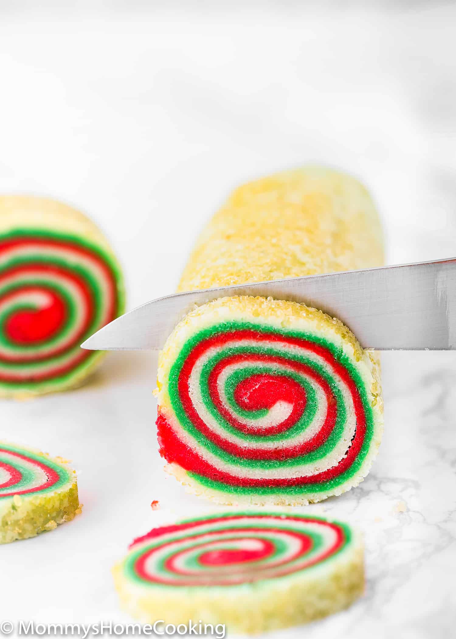 A knife cutting a Eggless Icebox Pinwheel Cookie Dough logs into slices..