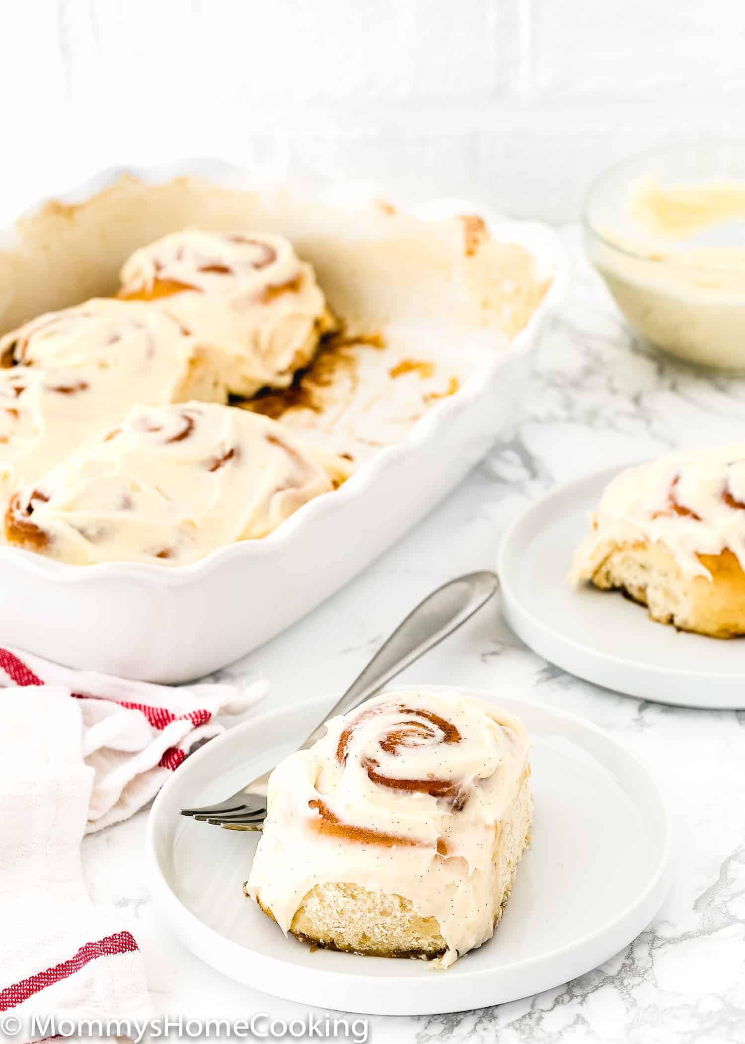 Eggless Cinnamon Roll on a plate with cream cheese frosting on top and a fork on the side