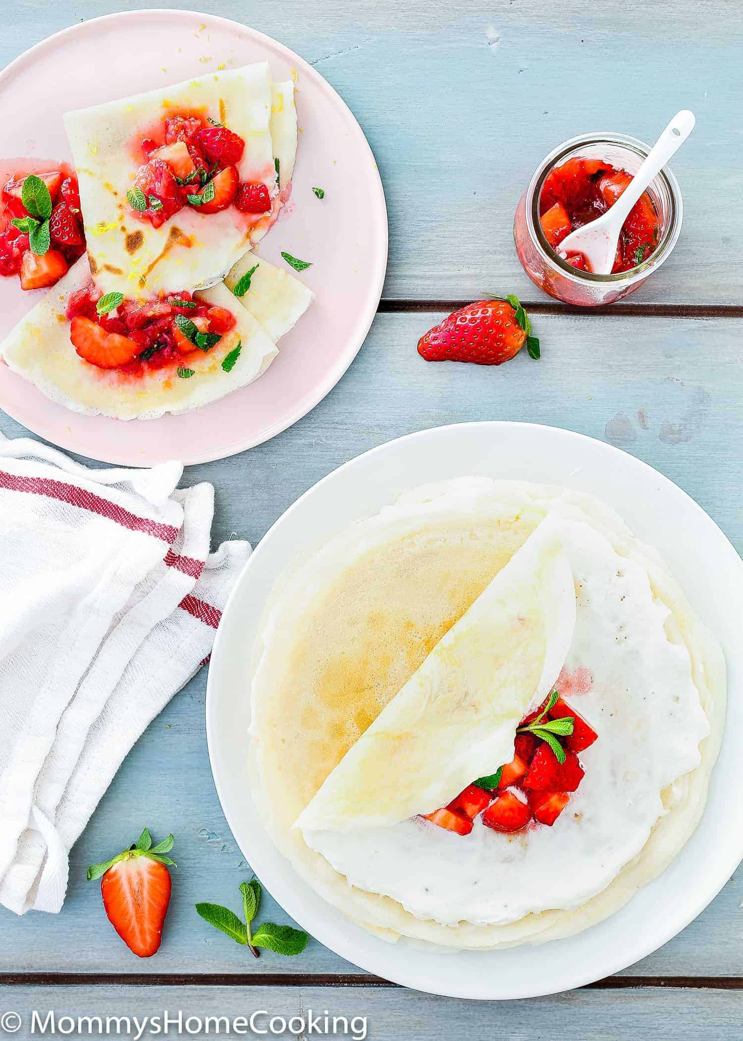 Overhead view of two plates with eggless crepes on them. Strawberries on top as garnish.