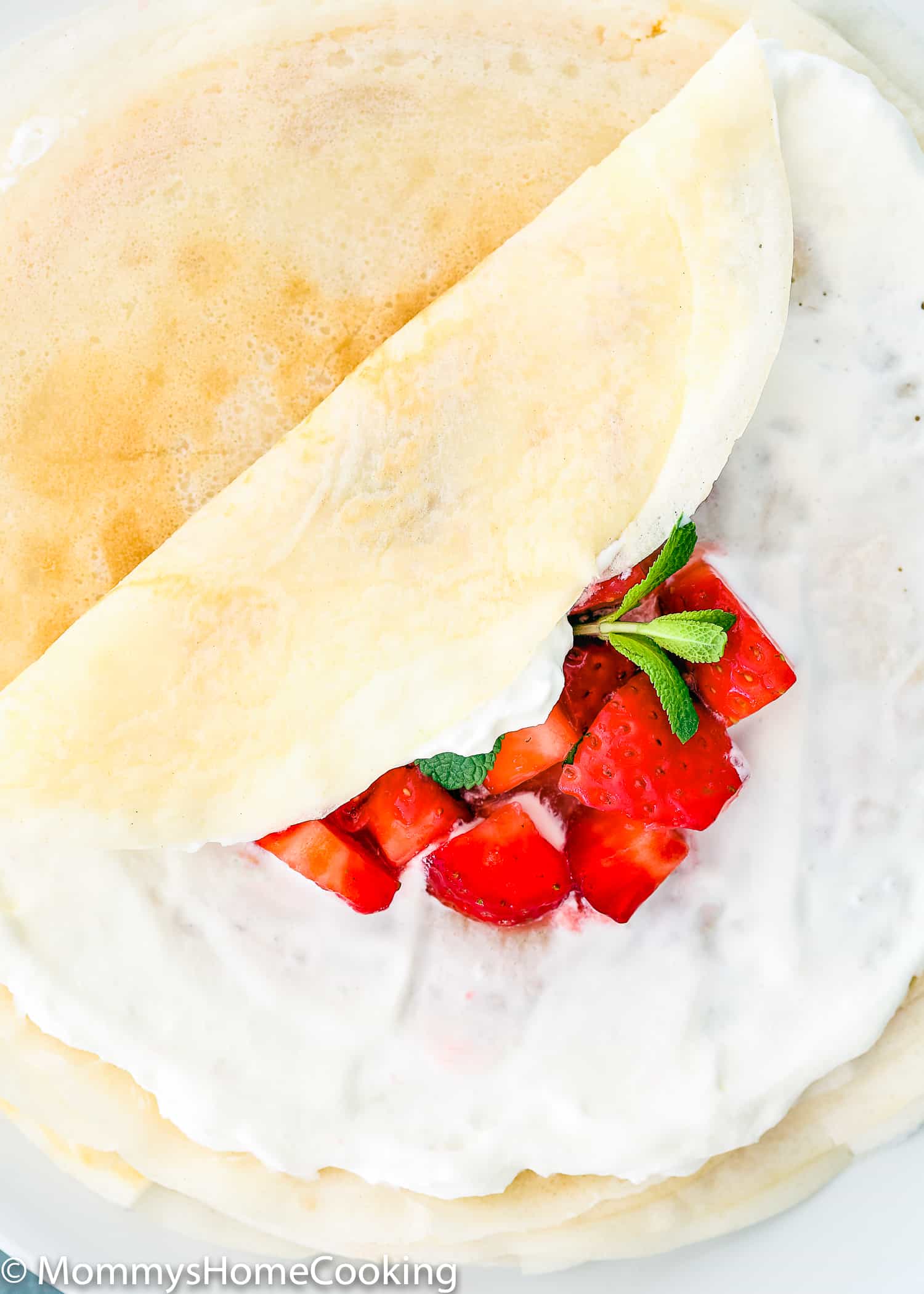 A stack of eggless crepes with one folded with strawberries inside.