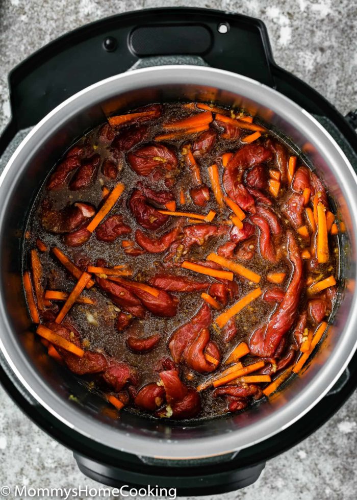 An open pressure cooker reveals an easy Instant Pot Mongolian beef dish with sliced beef and thin carrot strips soaking in a rich brown sauce.
