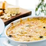 cheesy gnocchi casserole over a table with wooden cheese board
