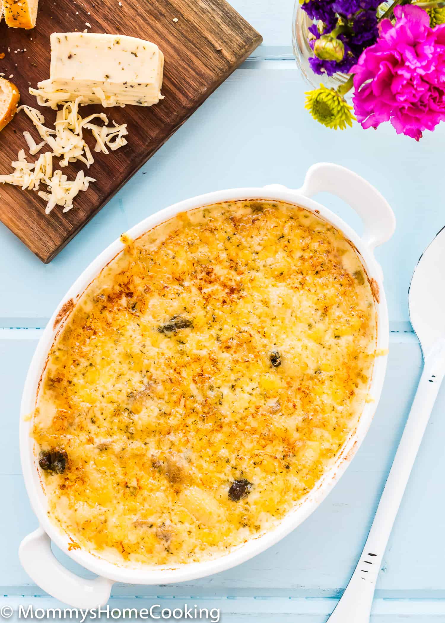 Cheesy Gnocchi Casserole over a wooden table with flowers and a cheese board