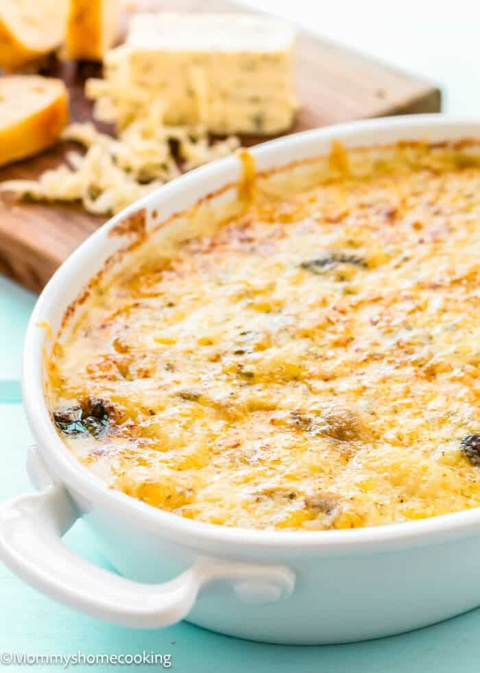 Golden-brown Cheesy Gnocchi Casserole (Skillet Recipe) baked in a white ceramic dish, with bread slices and melted cheese on a wooden board in the background.