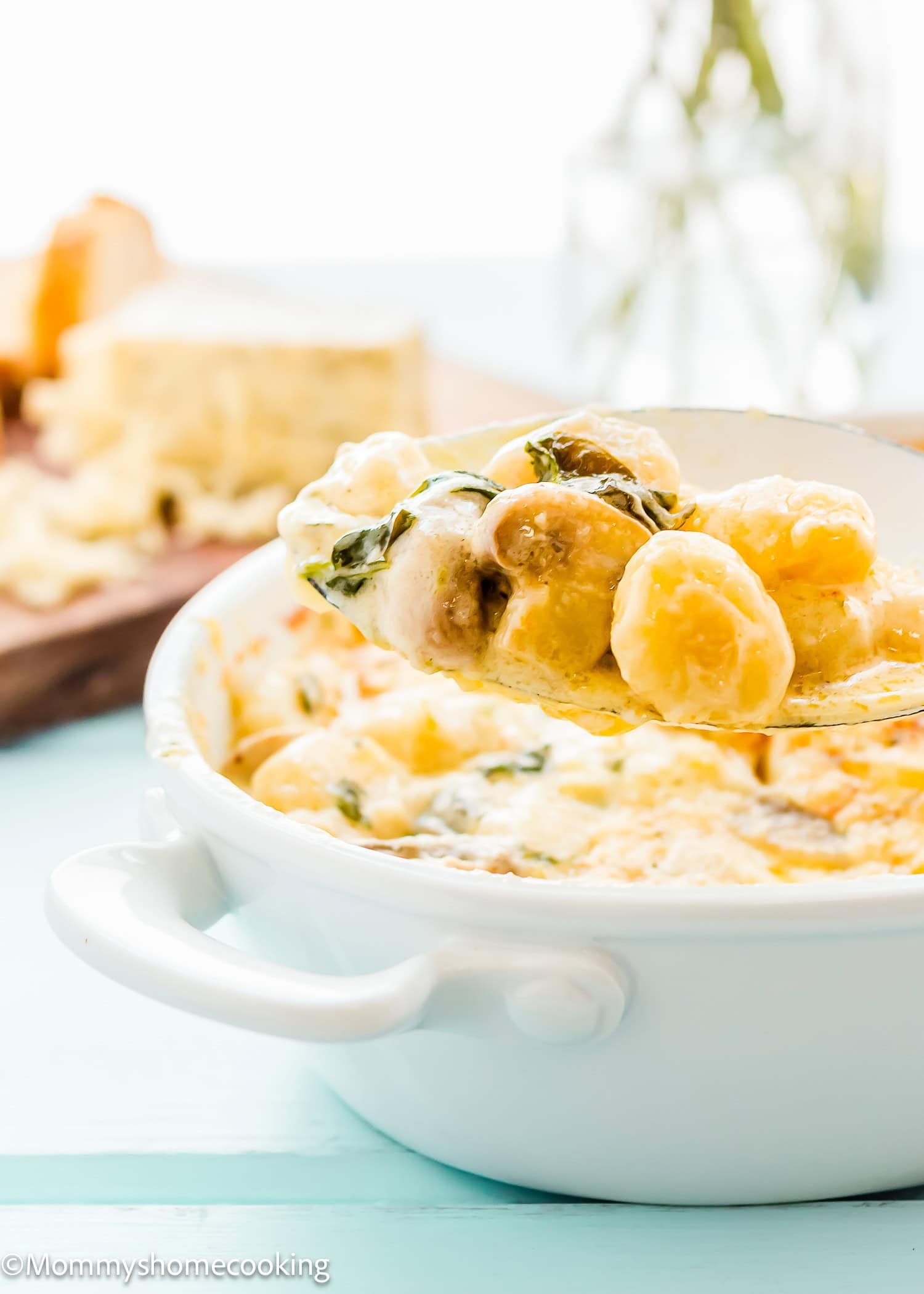 A spoonful of cheesy gnocchi casserole with spinach and mushrooms is lifted from a white casserole dish, showcasing this creamy skillet recipe.
