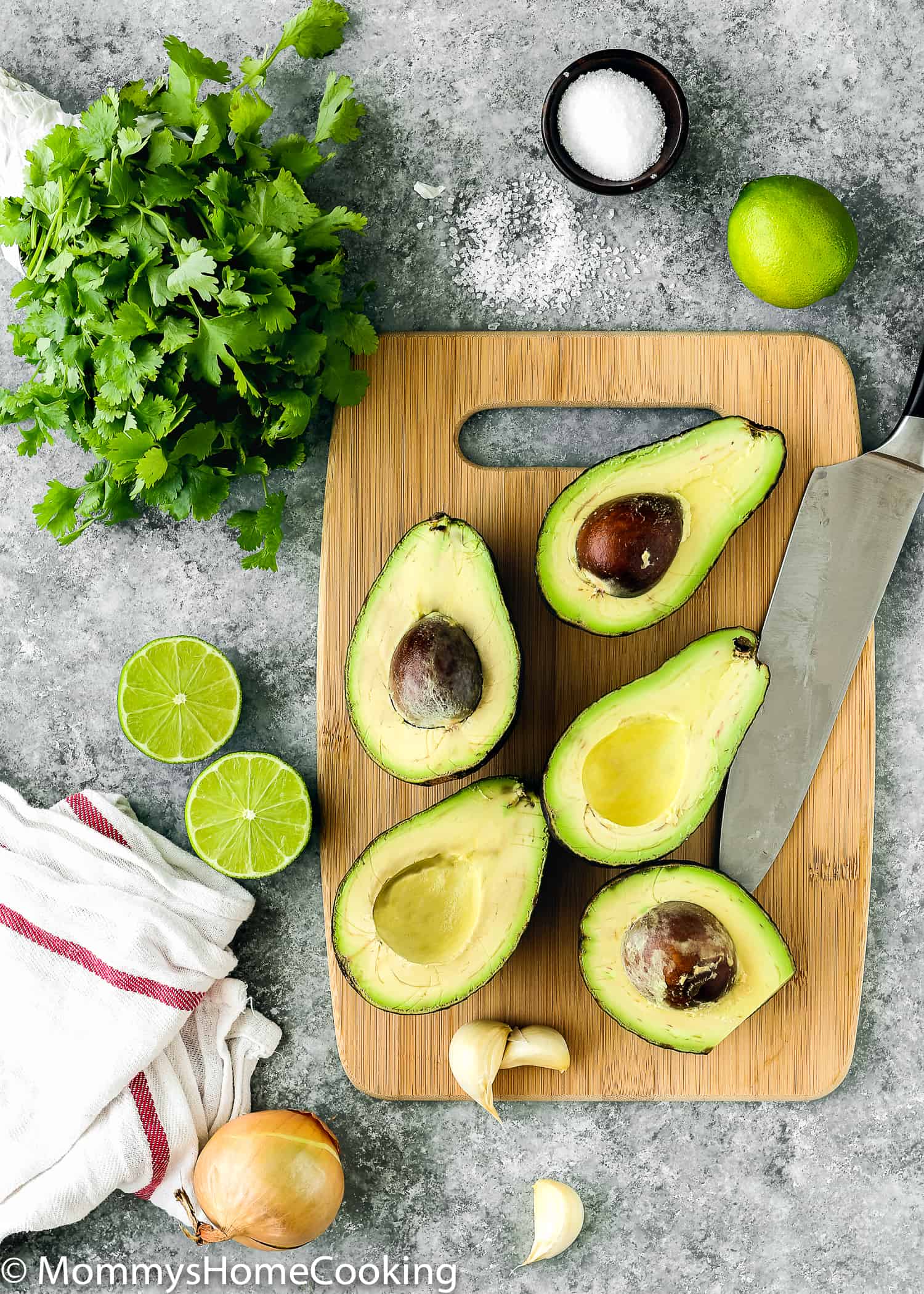 cut avocados on a cutting board and knife, onion, limes and cilantro.