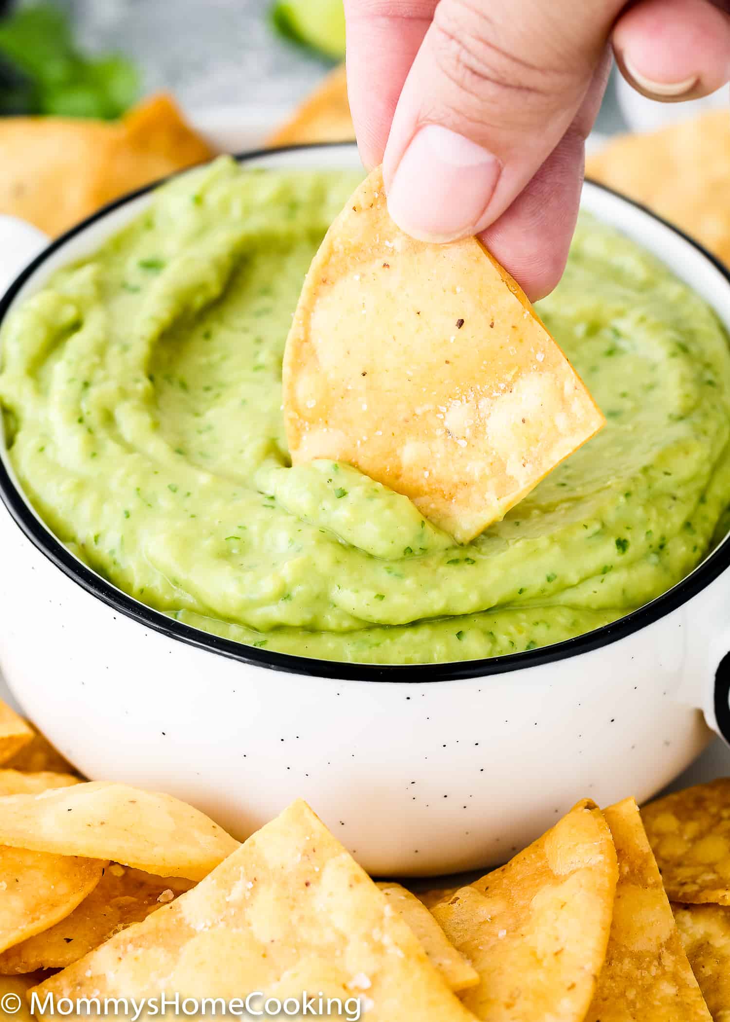 hand dipping a tortilla chip in avocado sauce.