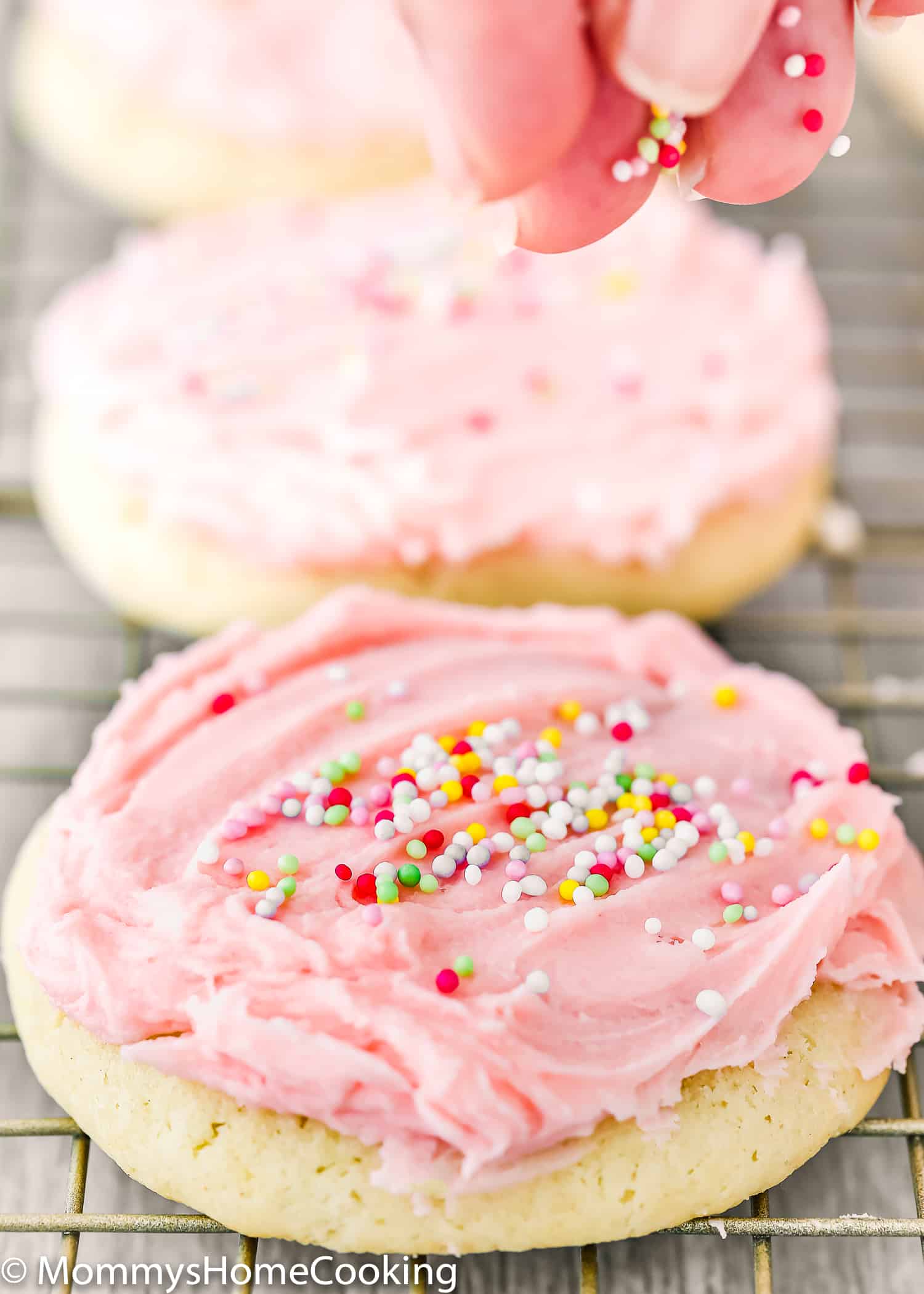 eggless sugar cookies frosted with pink buttercream and sprinkle over a cooling rack.