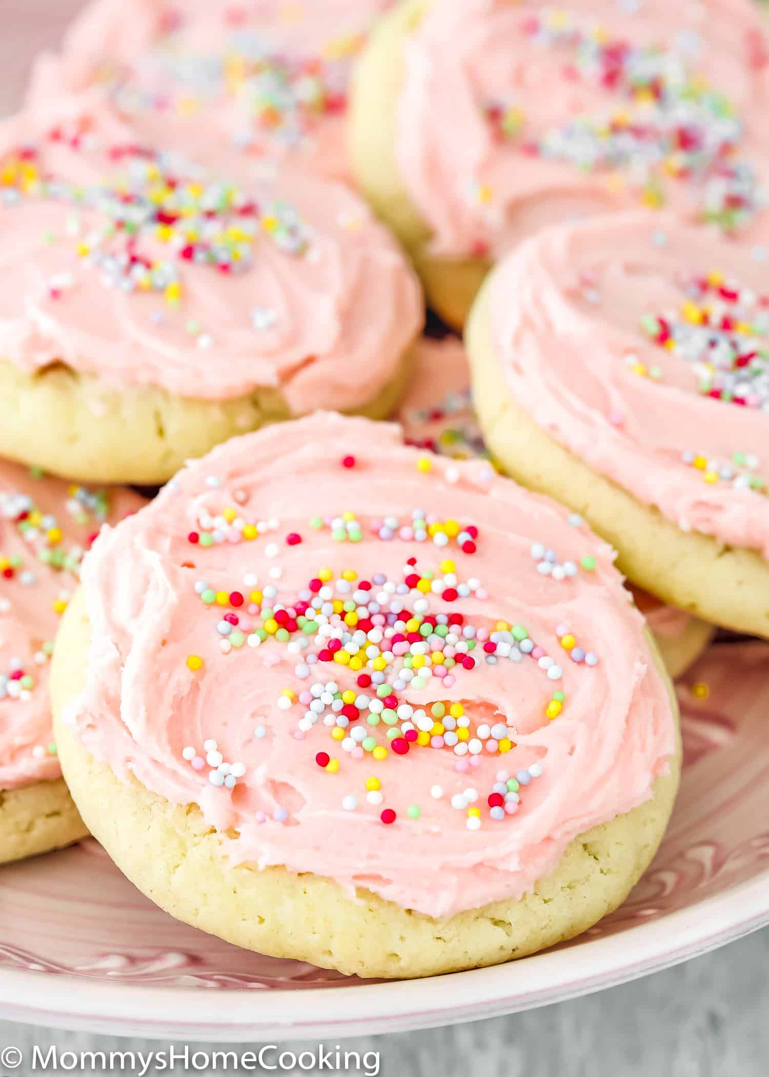 A plate with eggless sugar cookies frosted with pink buttercream and sprinkle.