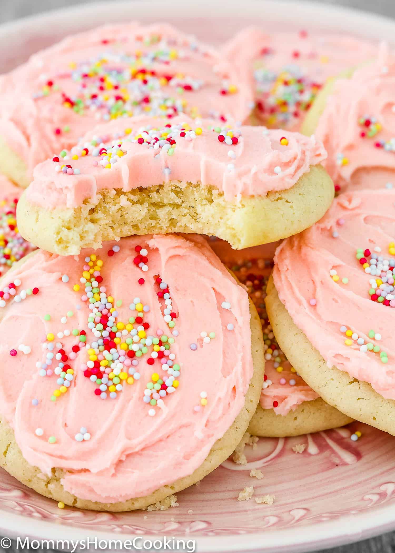 A plate with eggless sugar cookies frosted with pink buttercream and sprinkle.