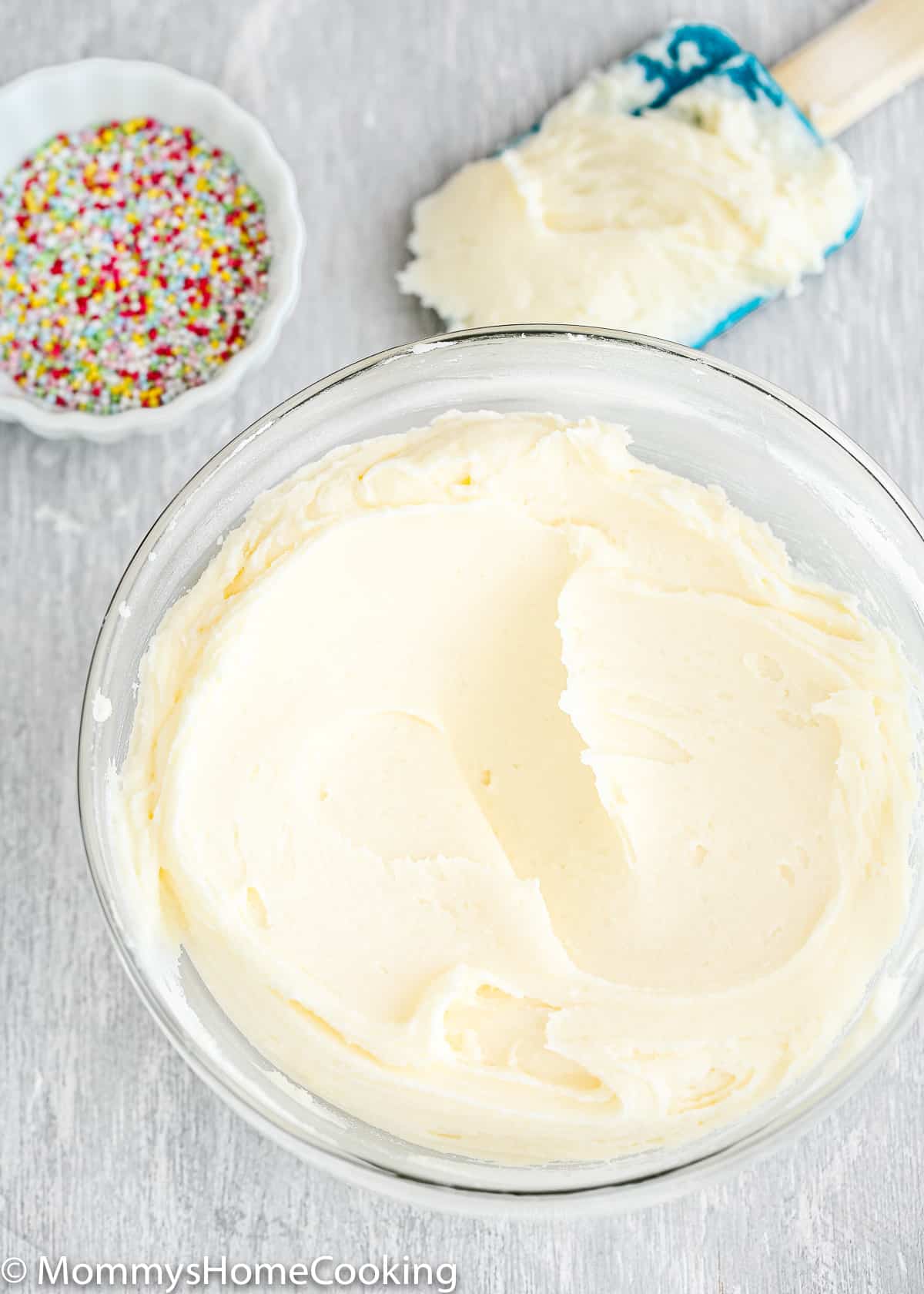 Vanilla Buttercream Frosting in a bowl with sprinkles and a spatula on the sides.