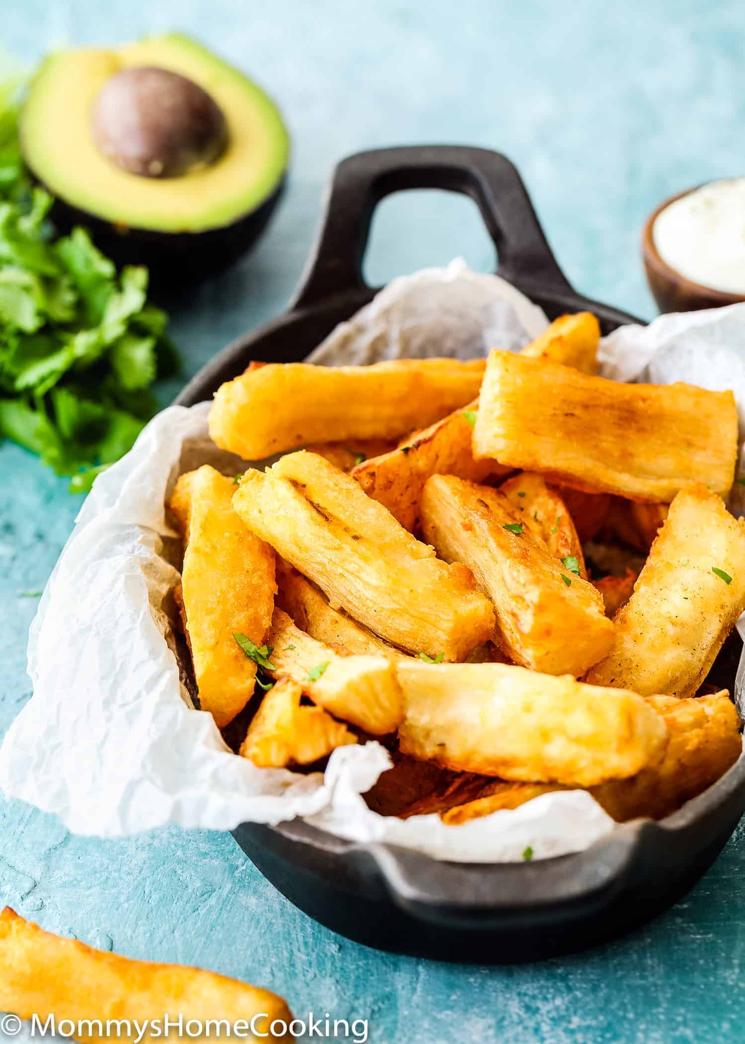 plate with yucca fries beside sauce and half avocado.