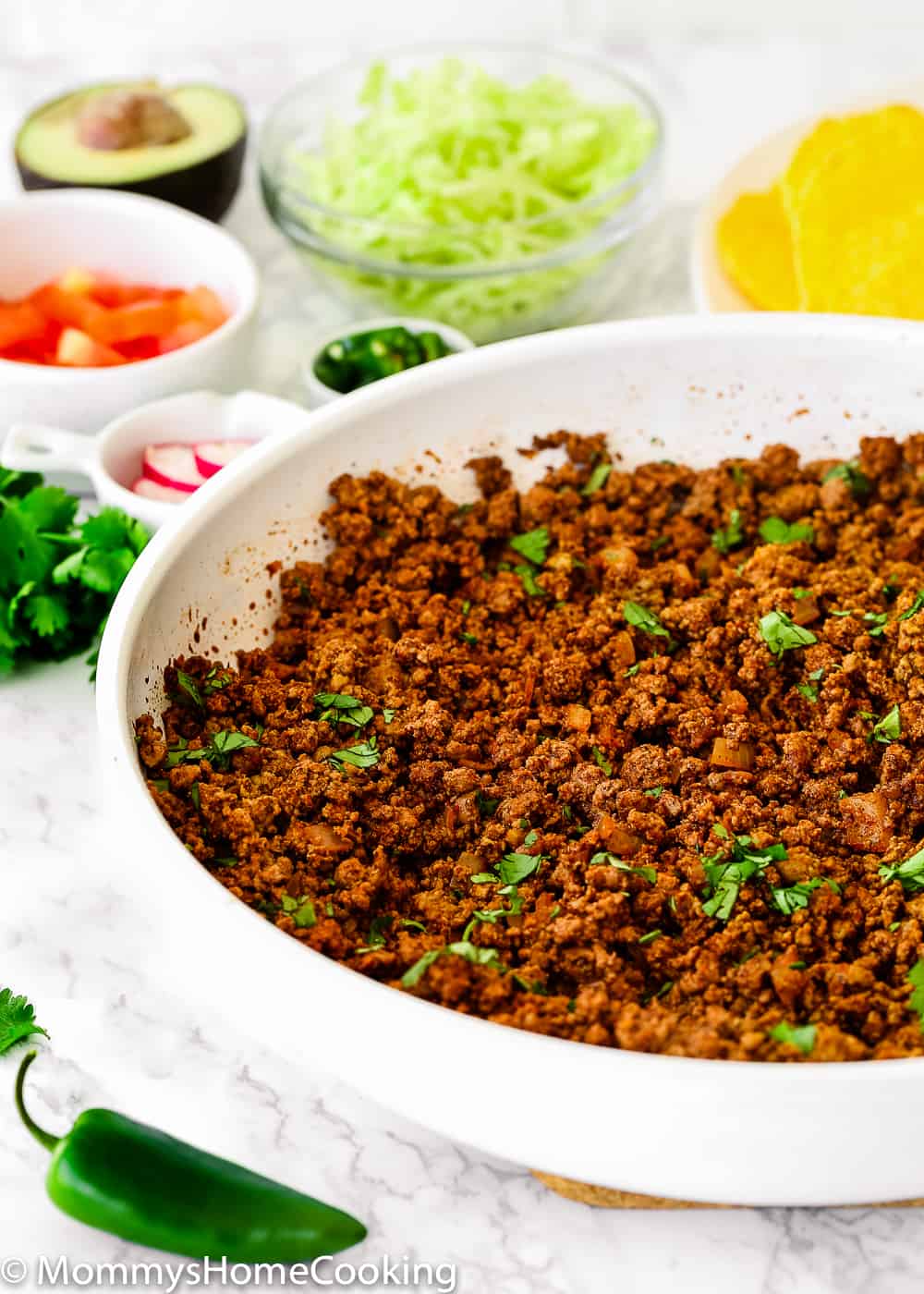 Cooked Ground Beef for Tacos in a white skillet  surrounded by taco toppings.