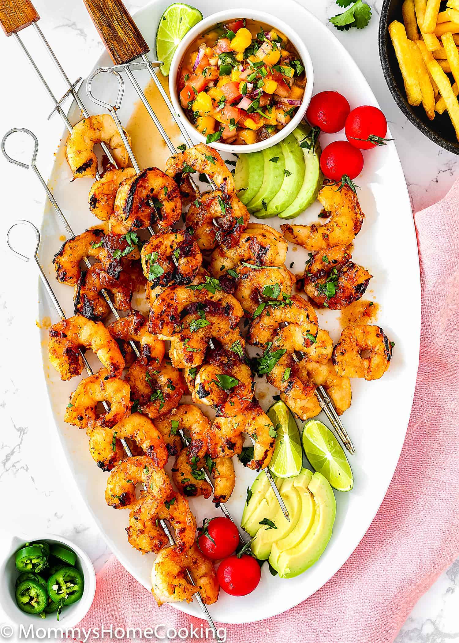 Honey Chipotle Grilled Shrimp in a white oval plate served with sliced avocado, cherry tomatoes and mango salsa