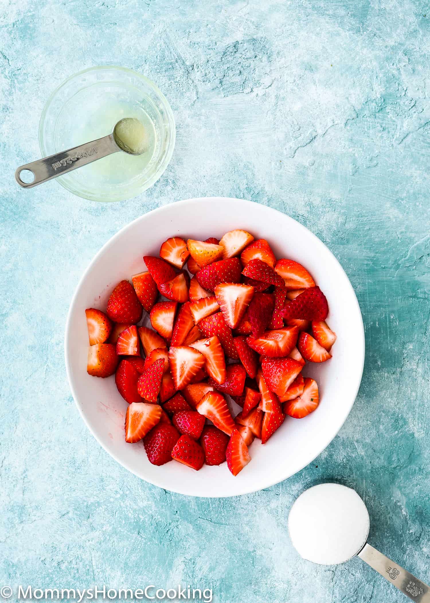 white bowl with chopped strawberries , bowl with lemon juice and a cup with sugar