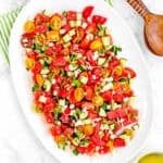 Easy Watermelon Summer Salad on a white serving plate over a green kitchen towel and dressing and serving spoons on the side.