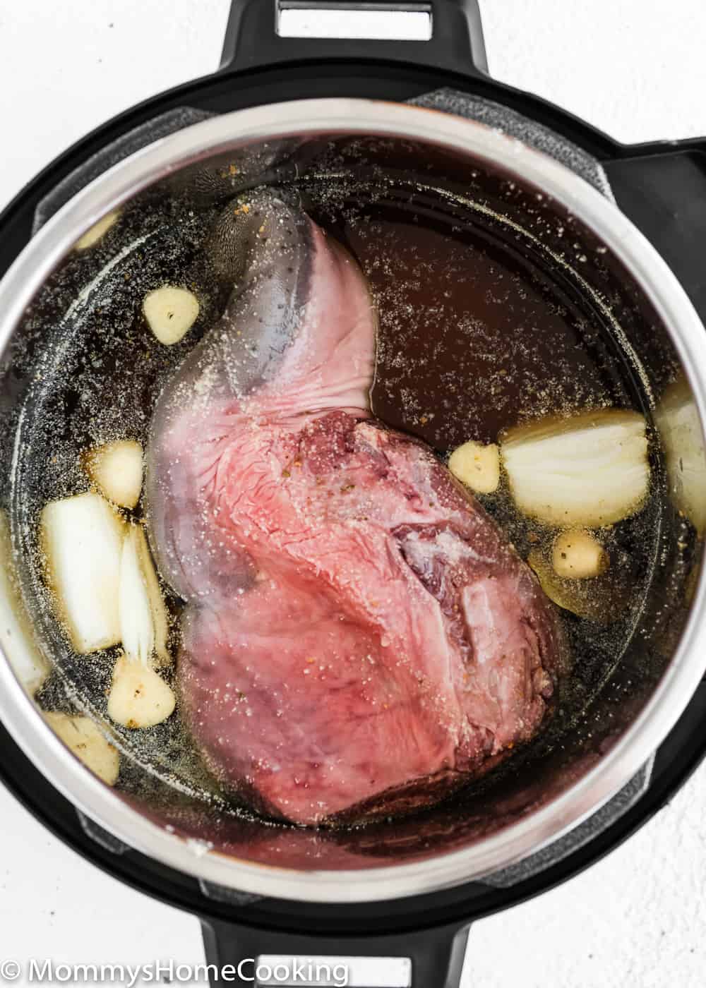 uncooked beef tongue in a pressure cooker with onion, garlic and bay leaf