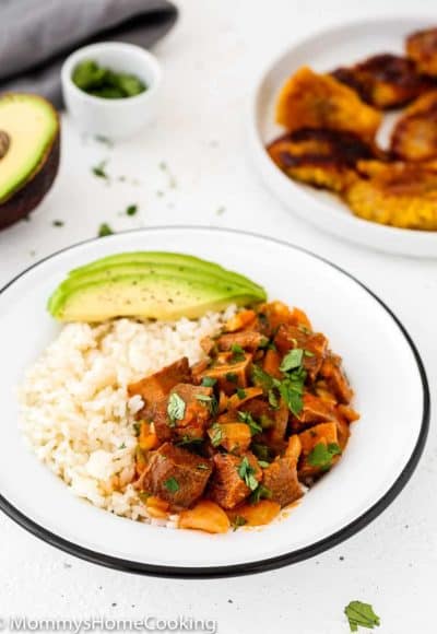 cooked Beef tongue in tomato sauce in a plate with sweet plantains, white rice and avocado