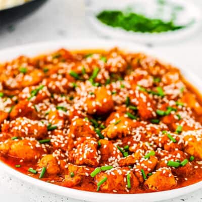 Korean Kimchi Chicken with sesame seeds and green onions on a plate.