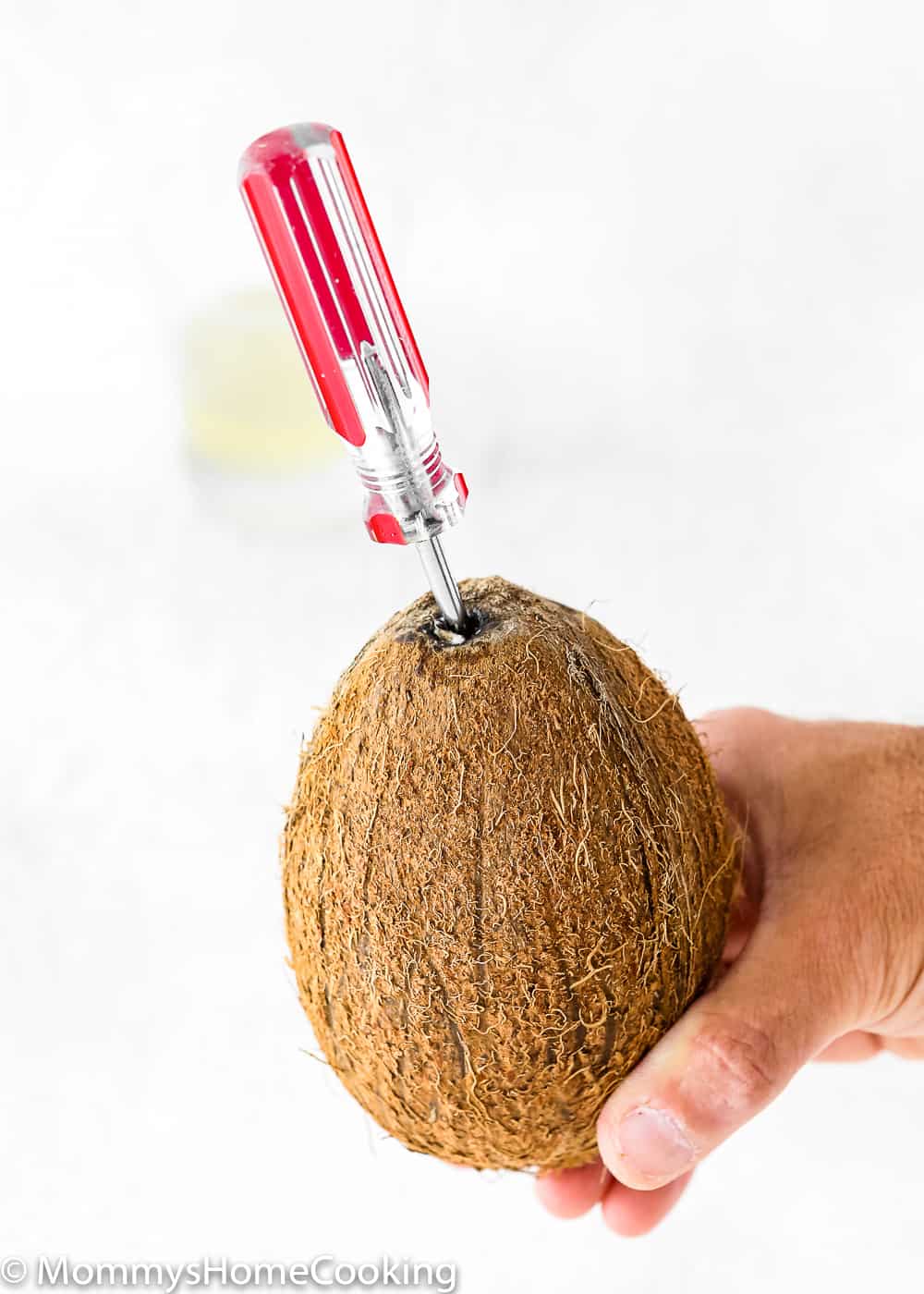 a hand holding a coconut with a screwdriver inserted in it. 