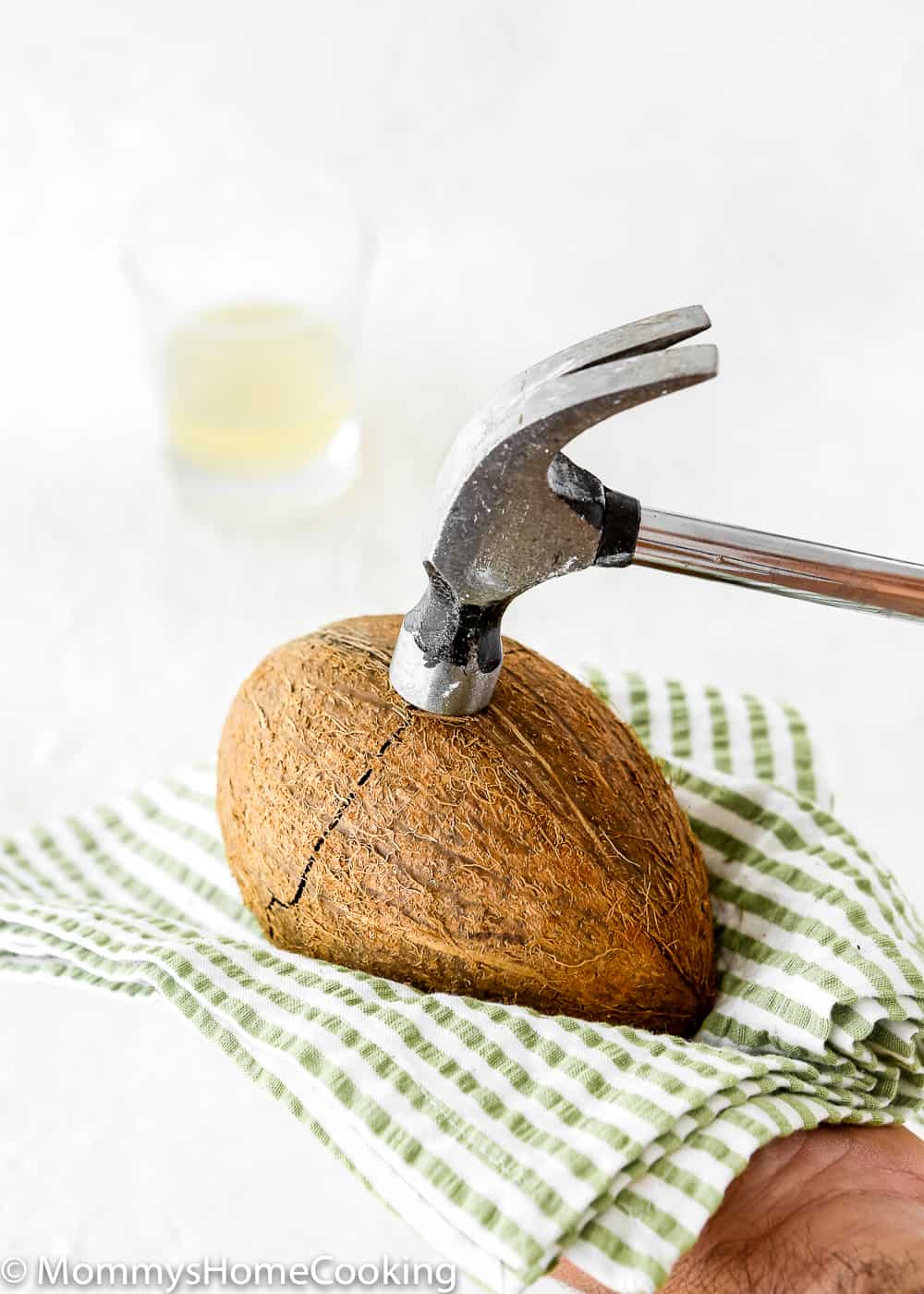 a hammer hitting a coconut over a kitchen towel. 