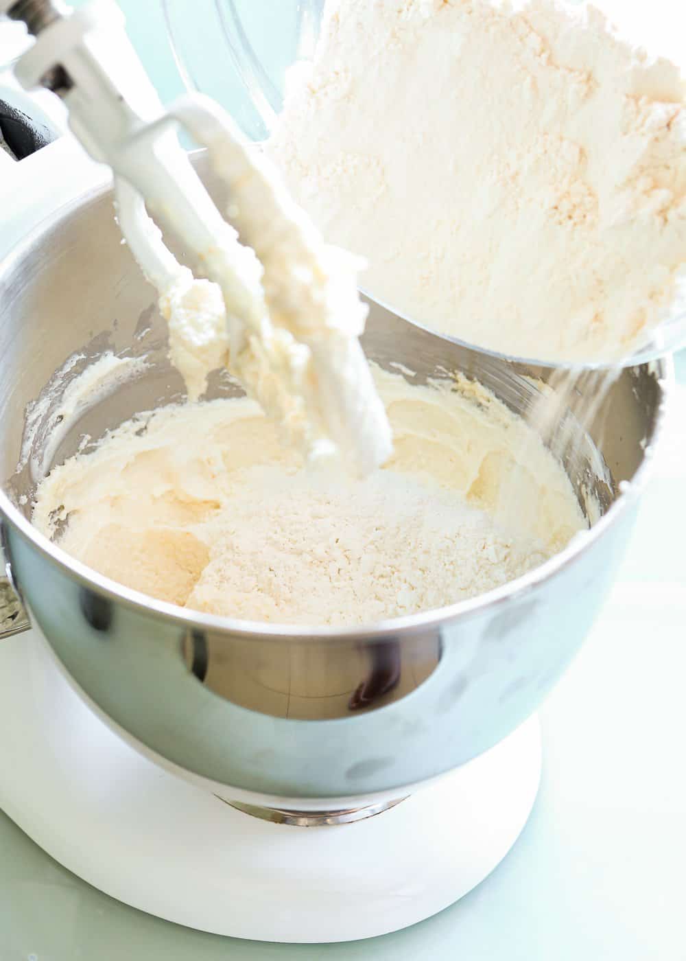 flour being added to a bowl of a stand mixer with butter and sugar creamed together.