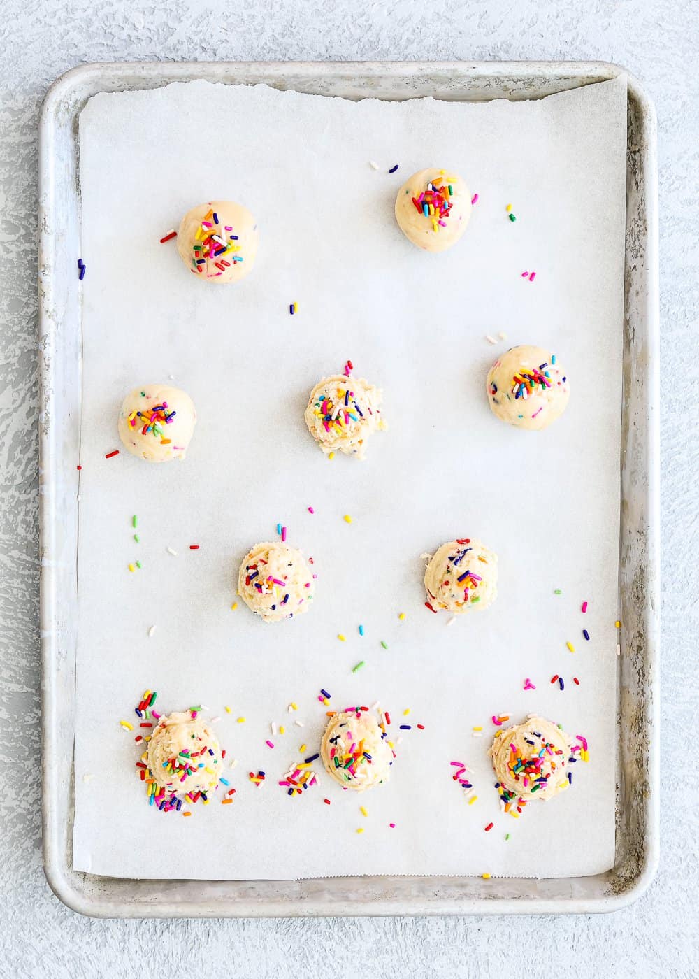 mounds of egg-free cookie dough in a baking sheet with sprinkles on top. 