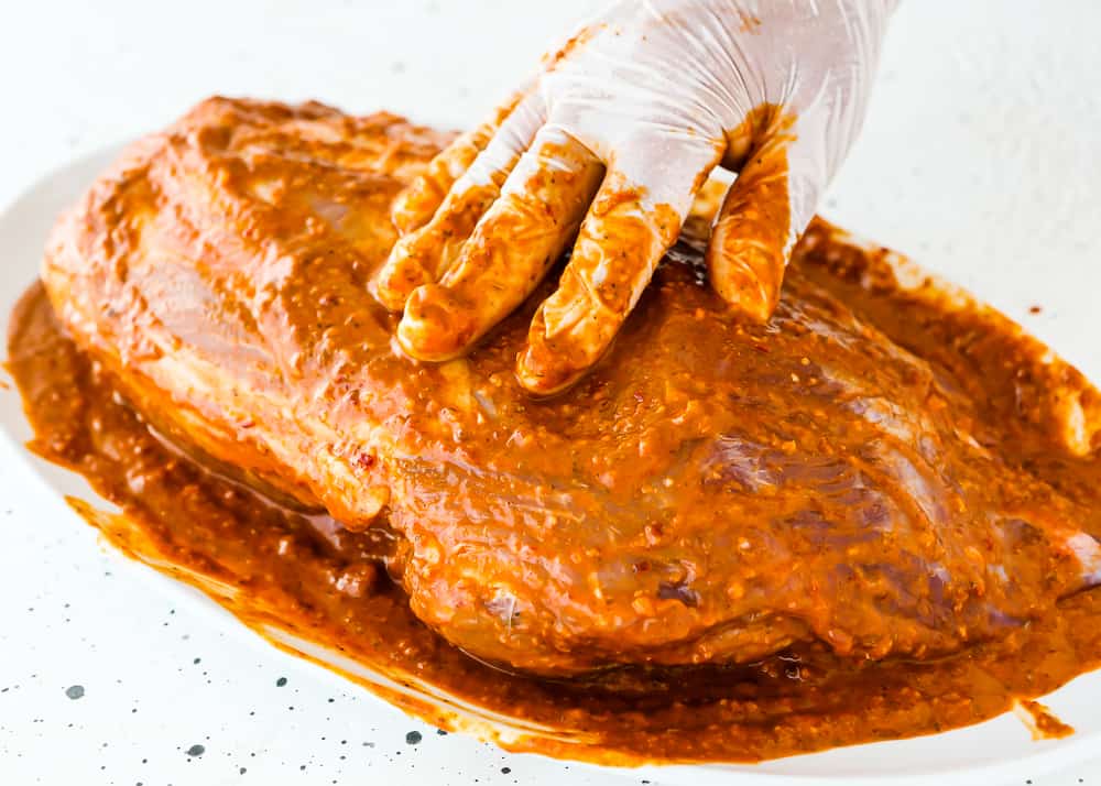 a hand rubbing a raw pork shoulder with chipotle sauce. 