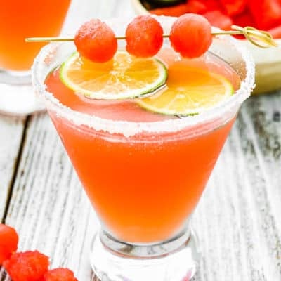 a Watermelon Cocktail in a cosmopolitan glass with watermelon balls and lime slices.