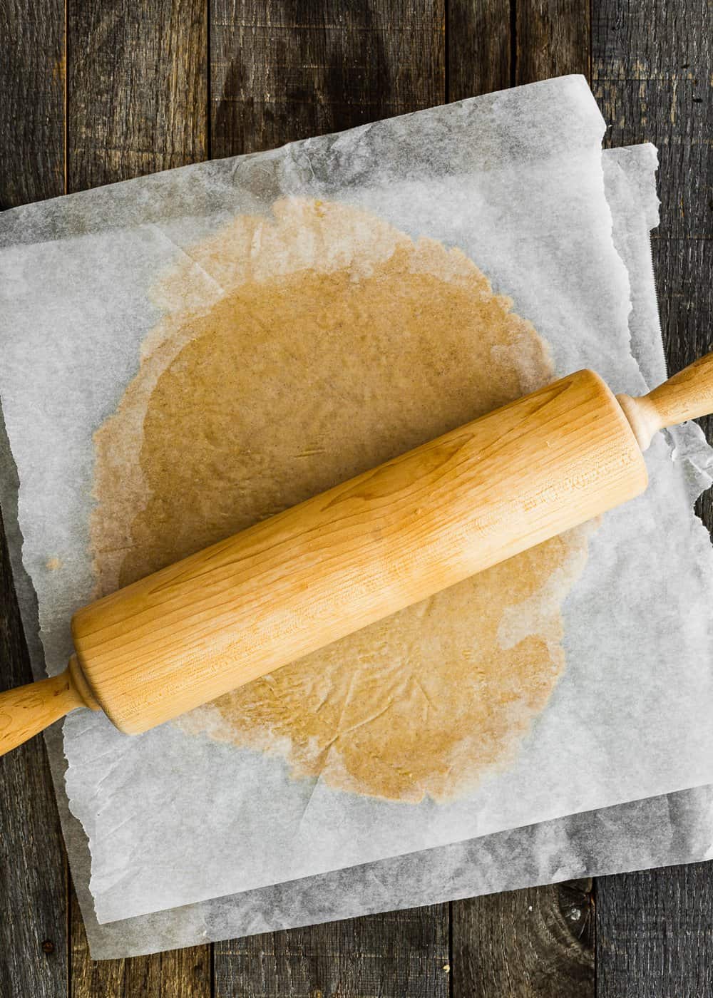 eggless cookie dough between two pieces of parchment paper with a rolling pin on top.