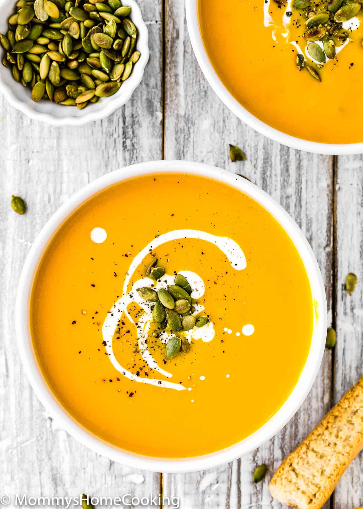 two bowls of pumpkin soup garnished with pepitas and cream
