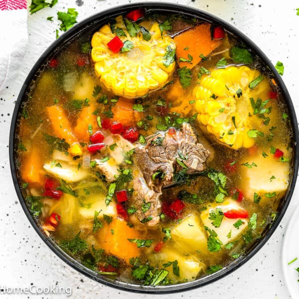 A bowl of Authentic Venezuelan Sancocho (Sancocho Venezolano) featuring beef, corn, carrots, potatoes, herbs, and red peppers in a clear broth, garnished with chopped cilantro.