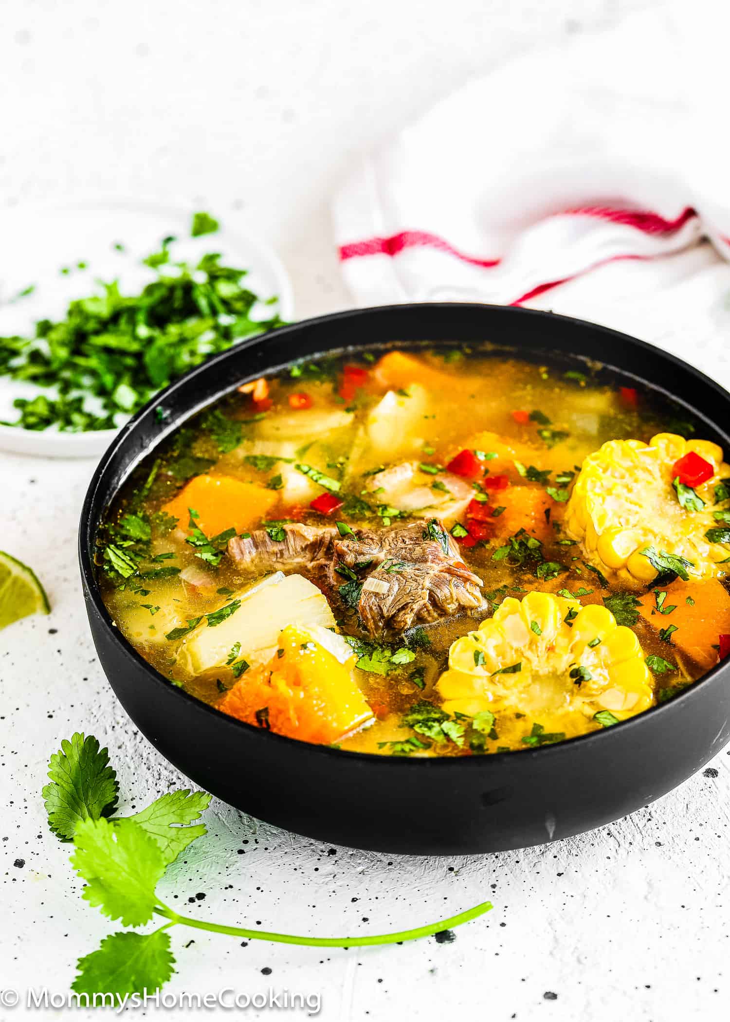 Venezuelan Sancocho in a black bowl with a lime wedge and chopped cilantro in the side.