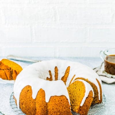 sliced Eggless Pumpkin Cake with glaze over a cooling rack with a cup of coffee in the background