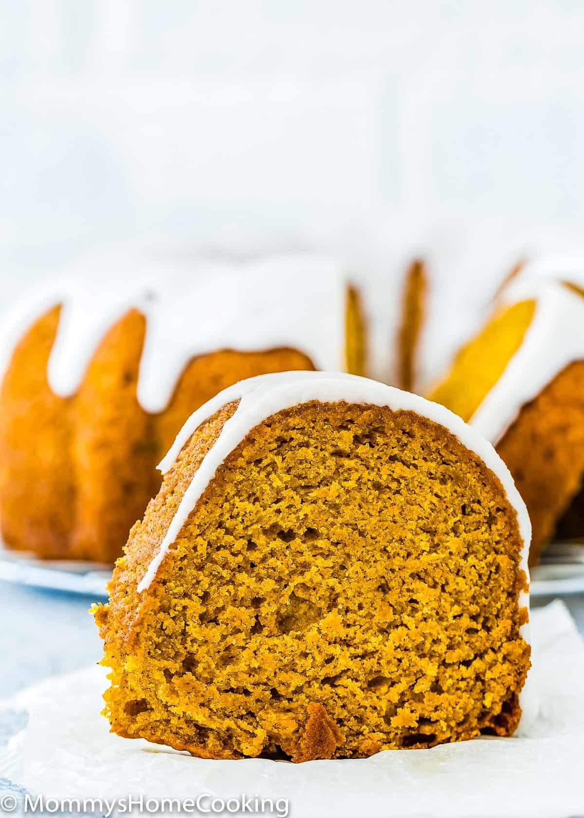 slice of Eggless Pumpkin Cake with glaze on a piece of parchment paper. 