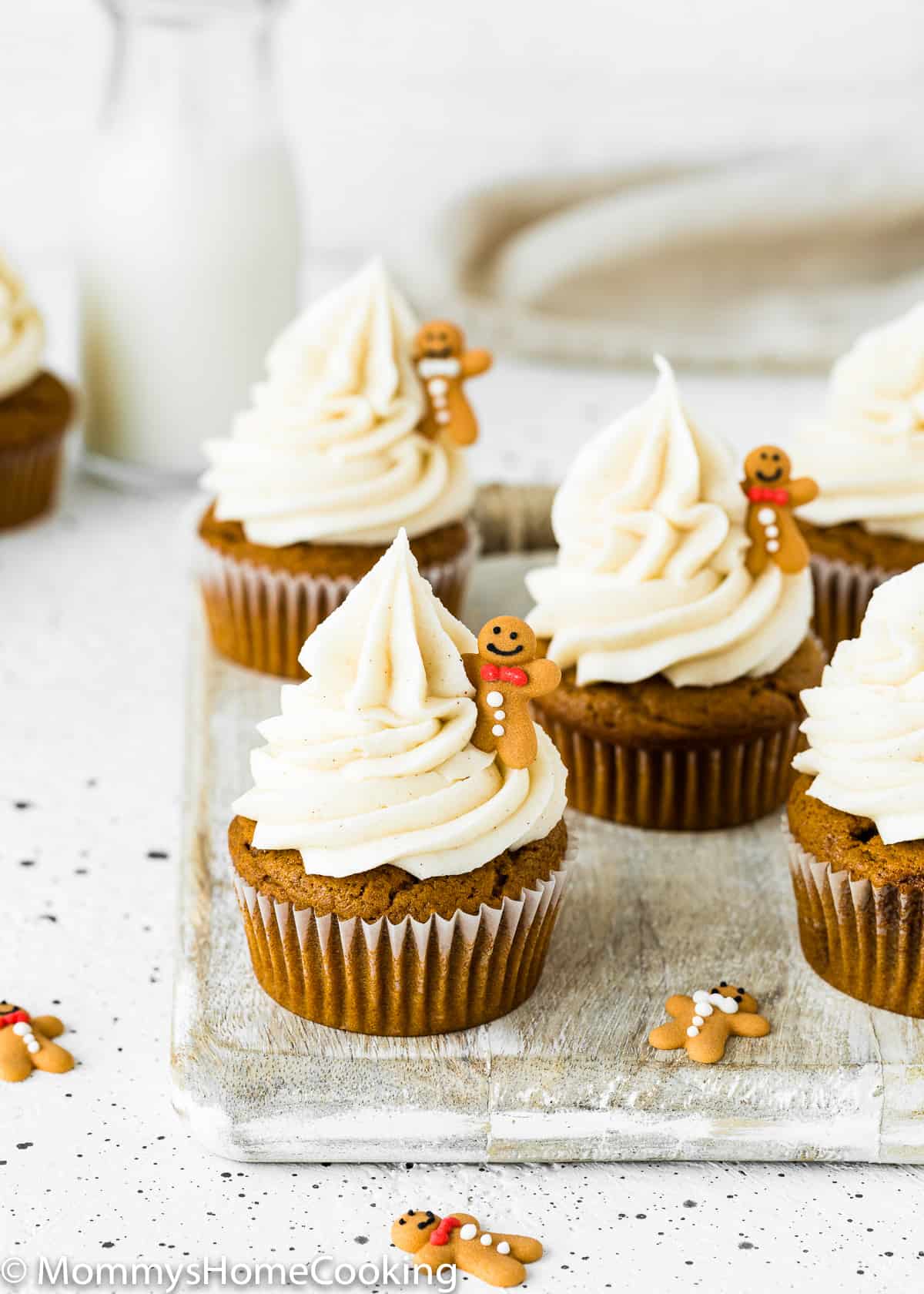 Eggless Gingerbread Cupcakes with cinnamon cream cheese frosting over a wooden surface with a bottle of milk in the background.