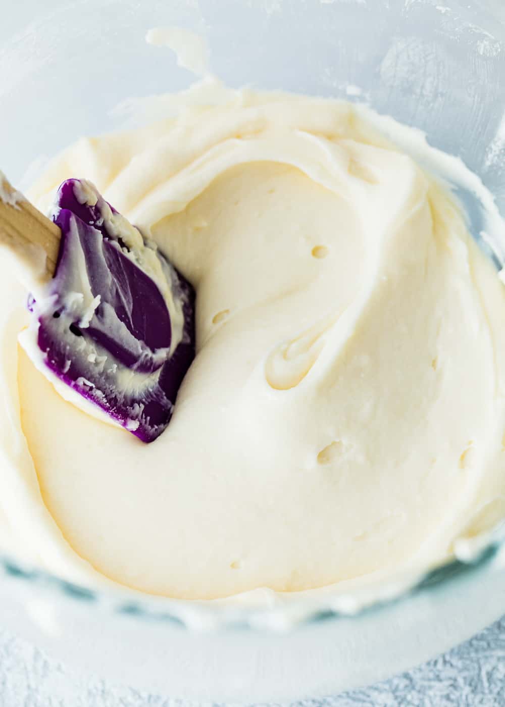 cream cheese frosting in a bowl with a Purple spatula