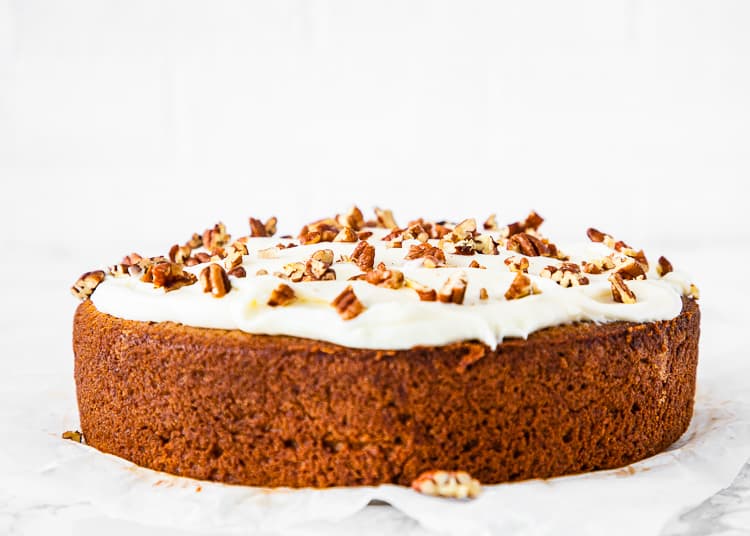 egg-free banana cake with cream cheese frosting and pecans on top over a marble surface. 