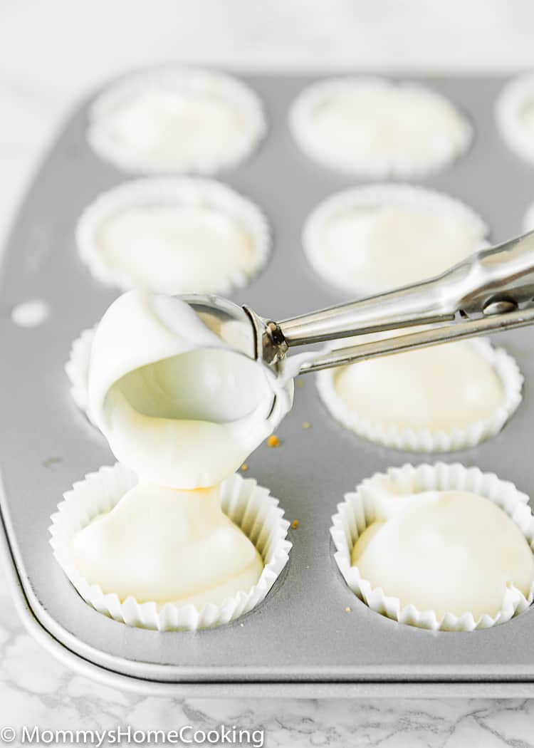 An ice cream spoon scooping egg-free cheesecake batter into a mini muffin cup. 