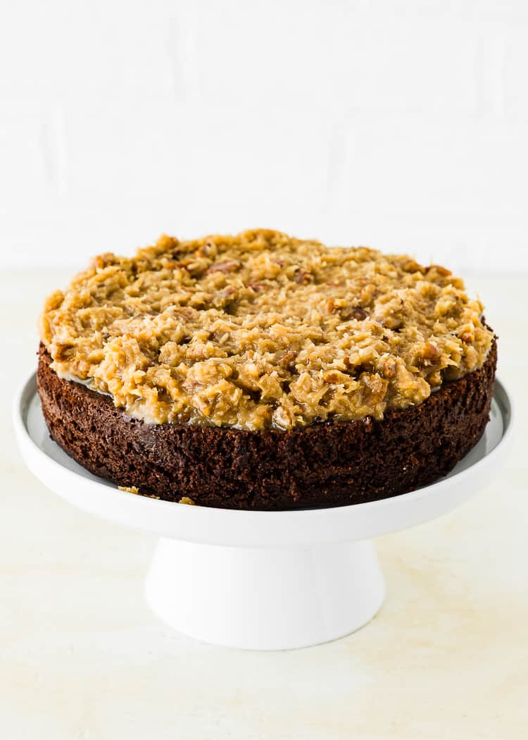 A layer of egg-free chocolate cake on a cake stand covered with eggless coconut pecan filling. 