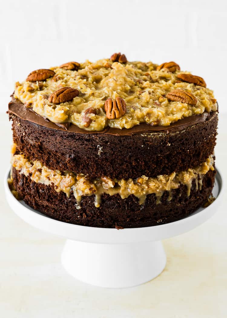 Two layers of egg-free german chocolate cake on a cake stand decorated with pecan on top.